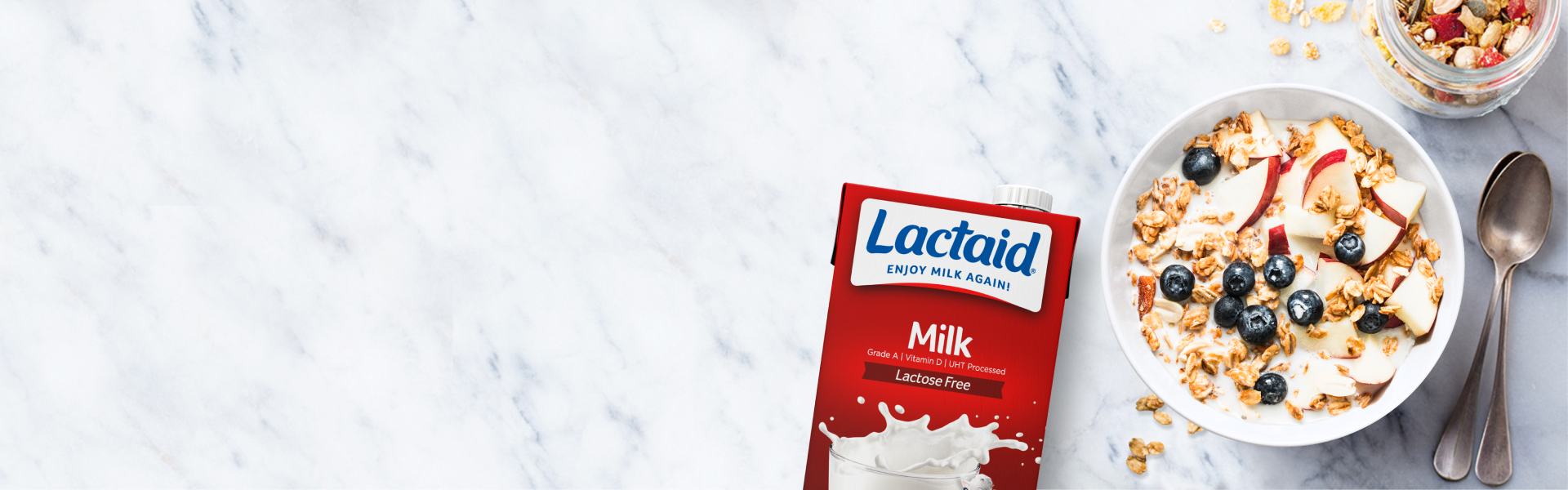 Caja de leche de larga duración sin lactosa de la marca LACTAID sobre una mesada, al lado de un recipiente con cereales y frutos rojos