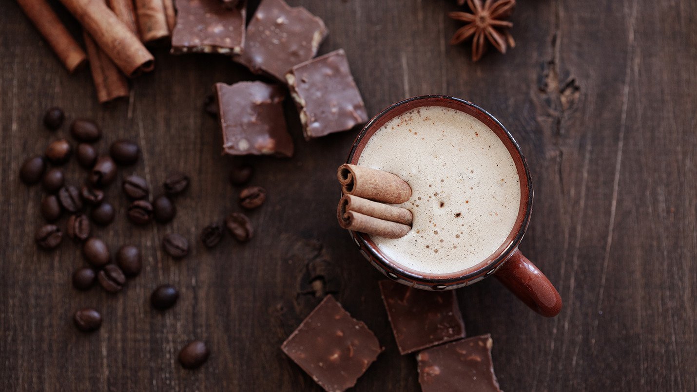 Café moca caliente con crema, ramitas de canela y trozos de chocolate
