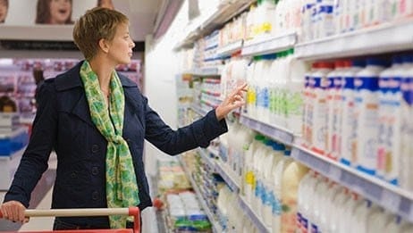 Una mujer de pelo corto y con una bufanda negra mirando la heladera de lácteos en una tienda de comestibles